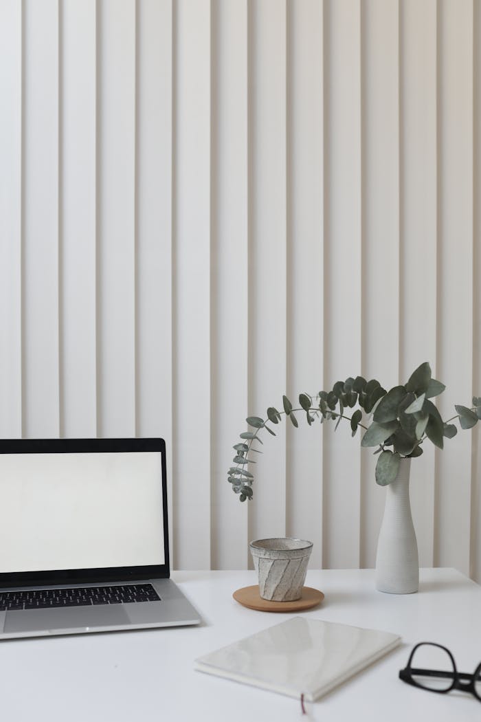 A clean and modern workspace featuring a laptop, vase with greenery, and notepad.